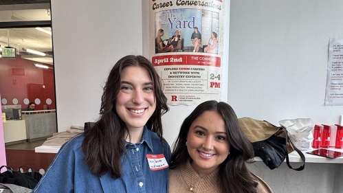 Two students posing in front of COMMchella poster