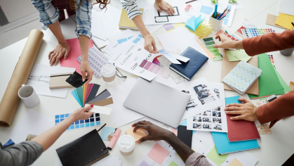 A group of individuals hovering over a worktable discussing various design elements for a project.