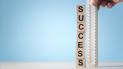 A hand holding a ruler against a tower of letter blocks spelling "success".