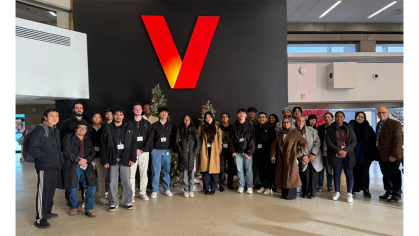 A group of SC&I students gather in front of the Verizon logo for a group photo while visiting Verizon on a class trip. 