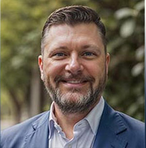 CPS faculty member Michael Lauer in a formal headshot. He's outside wearing a blue shirt and blue jacket and trees are in the background. 